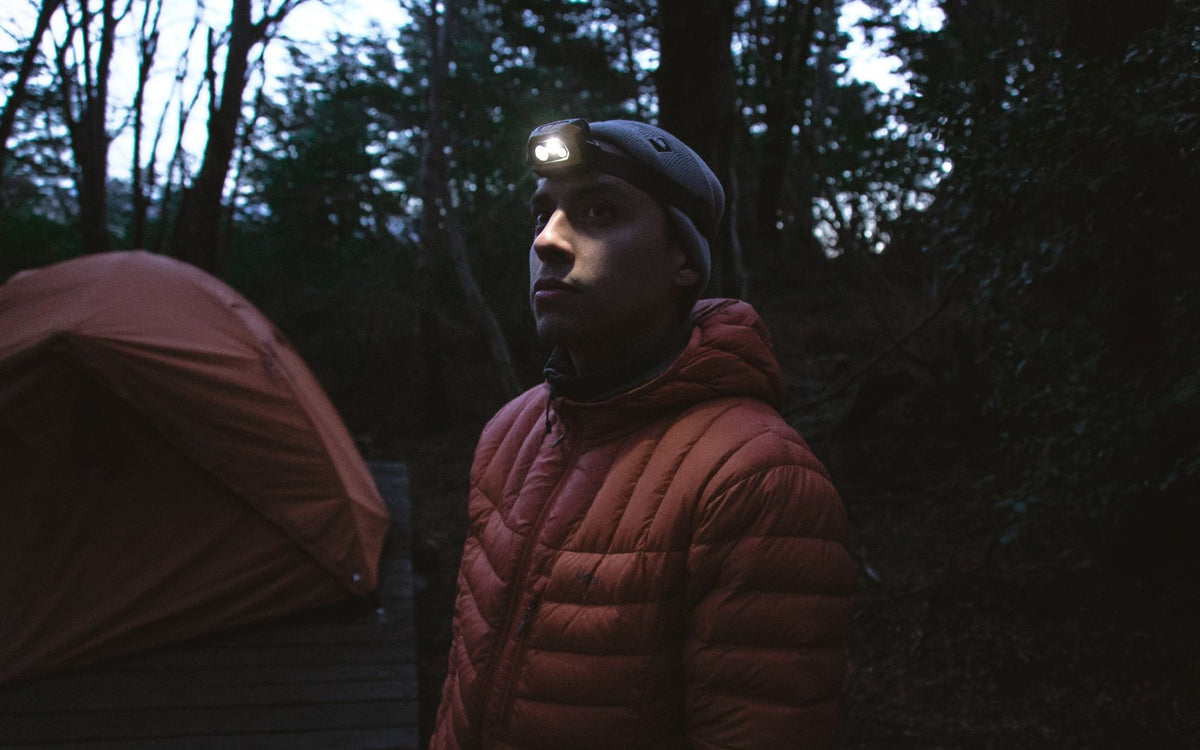 Camper wearing a headlamp next to a tent at dusk