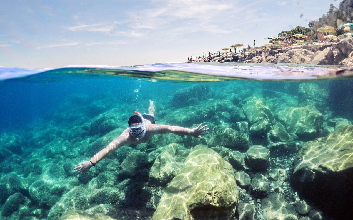 Snorkeller swimming over clear rocky seabed near the beach