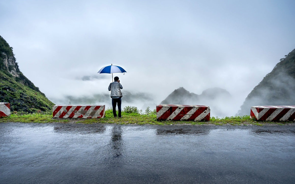 Traveller with an umbrella on a rainy mountain road